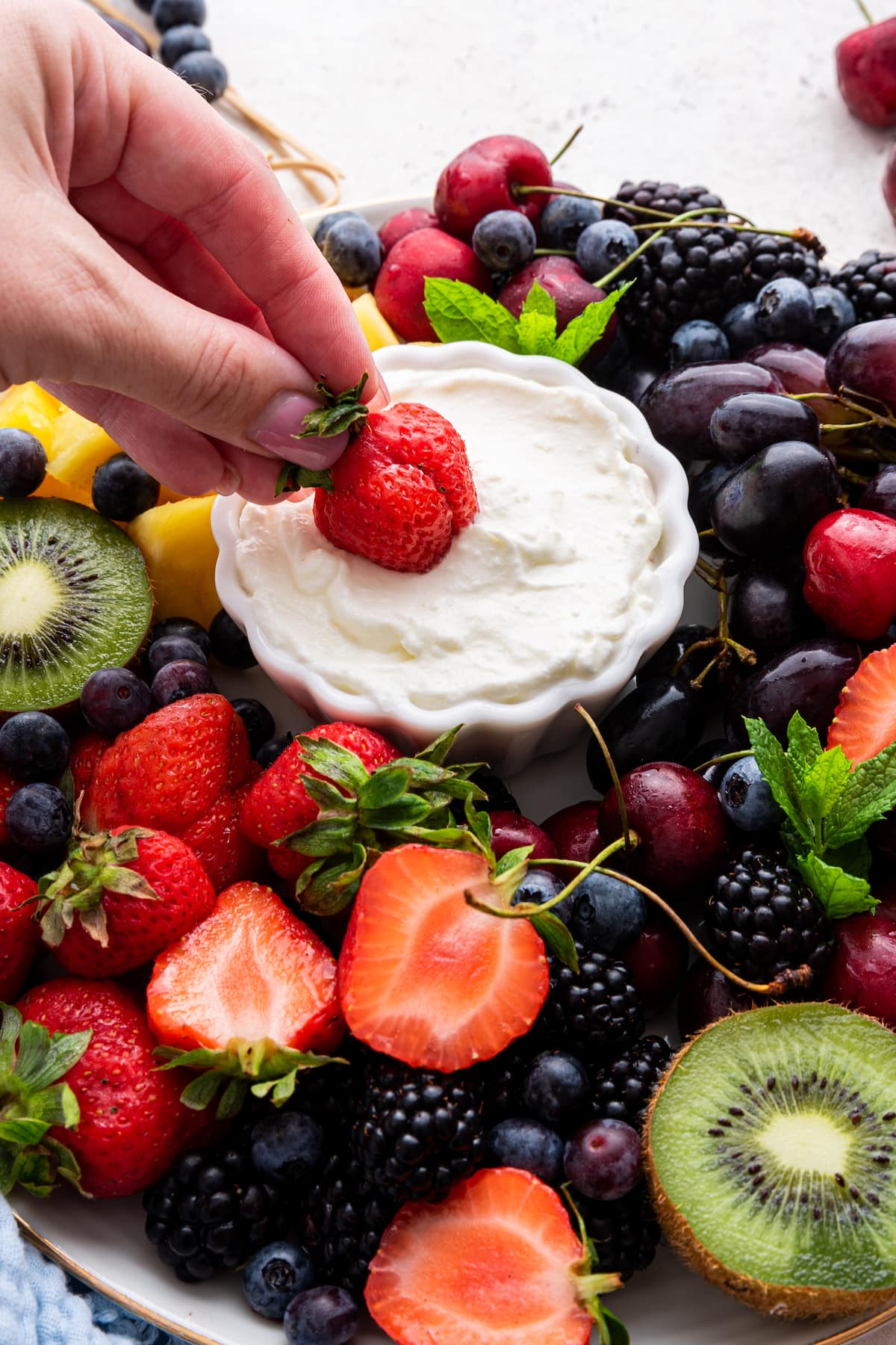 A woman's hand dipping a strawberry in the yogurt fruit dip.