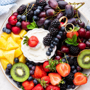 A white platter filled with a variety of fresh fruit with a yogurt fruit dip in the middle.