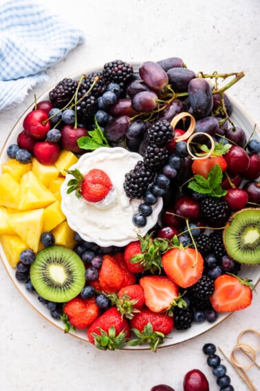 A white platter filled with a variety of fresh fruit with a yogurt fruit dip in the middle.