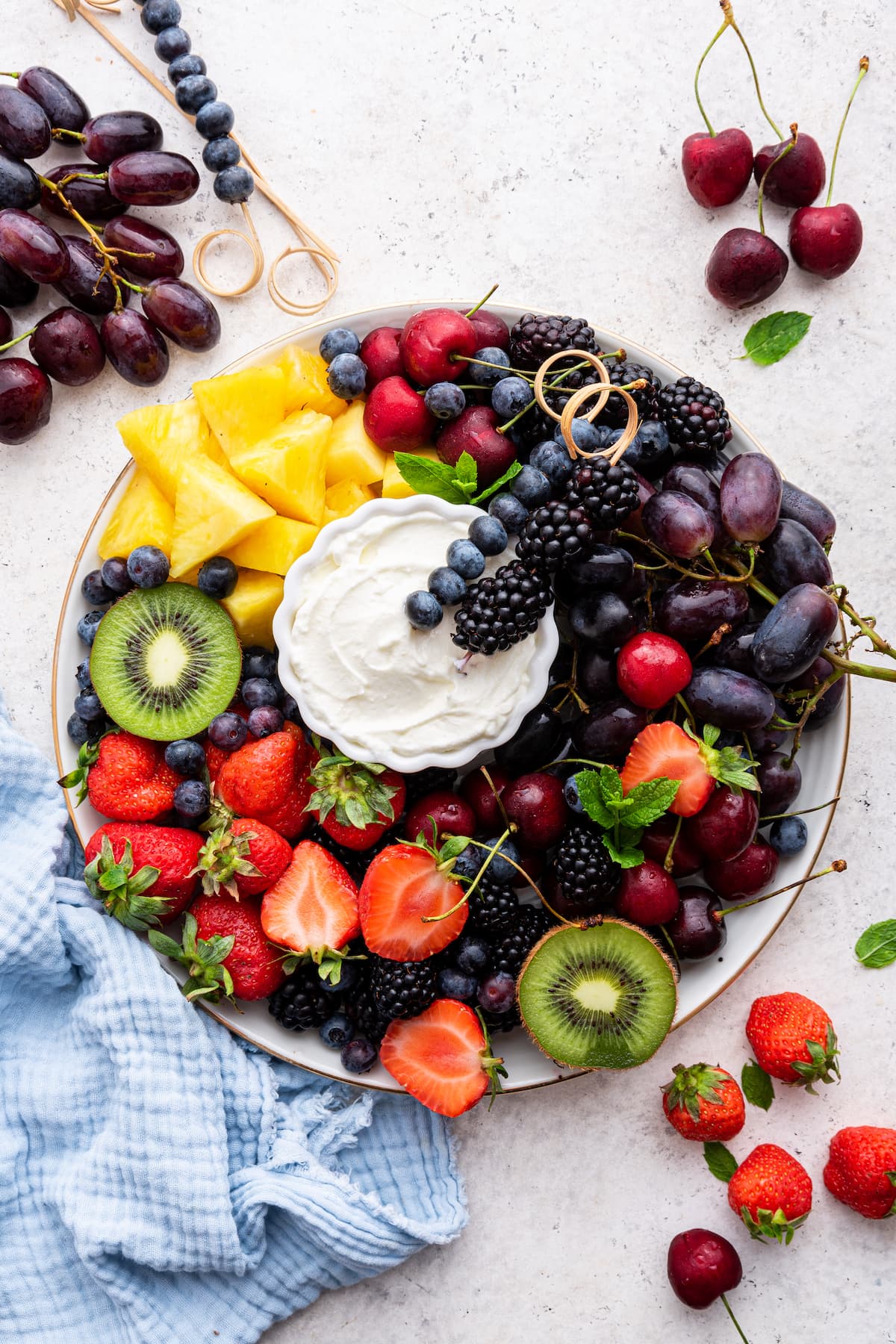 A white platter filled with a variety of fresh fruit with a yogurt fruit dip in the middle.