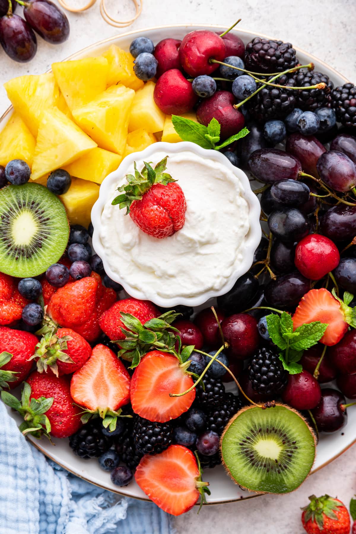 A white platter filled with a variety of fresh fruit with a yogurt fruit dip in the middle.