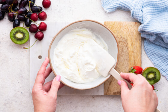 A woman's hands mixing the yogurt fruit dip in a white bowl.