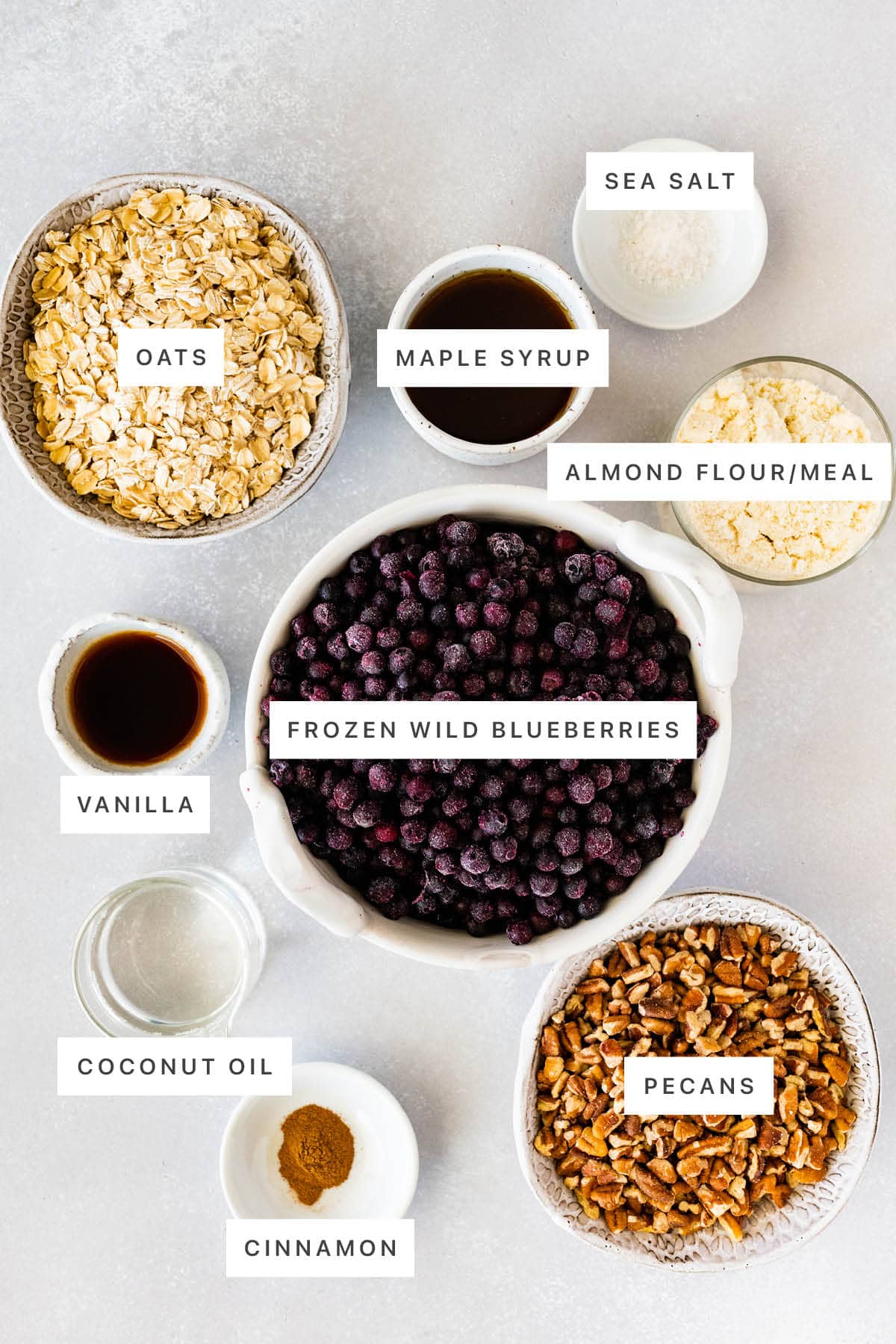Ingredients measured out to make Healthy Blueberry Crumble: oats, maple syrup, sea salt, almond flour/meal, vanilla, frozen wild blueberries, coconut oil, cinnamon and pecans.