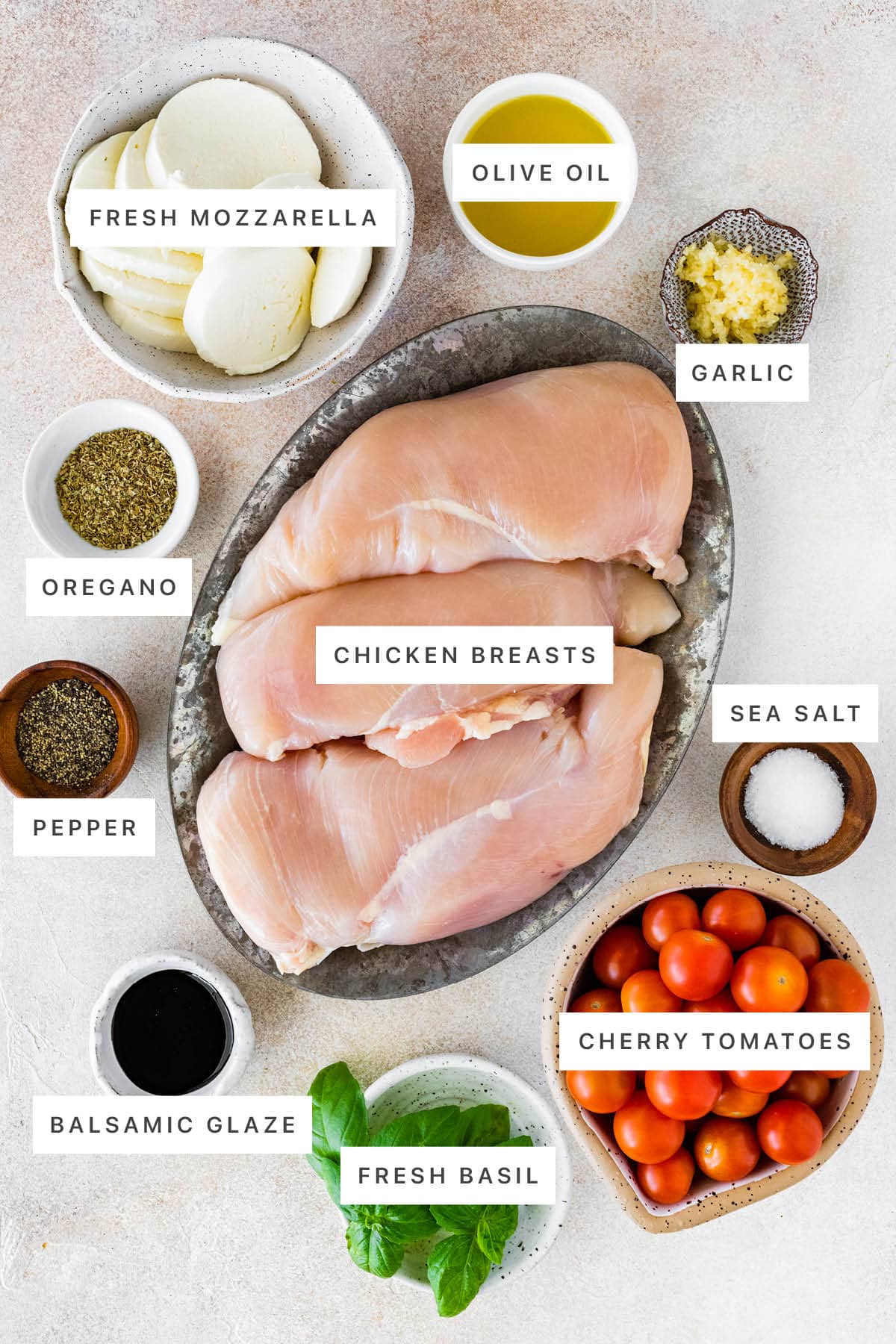 Ingredients measured out to make Baked Caprese Chicken: fresh mozzarella, olive oil, garlic, oregano, chicken breasts, pepper, sea salt, balsamic glaze, fresh basil and cherry tomatoes.