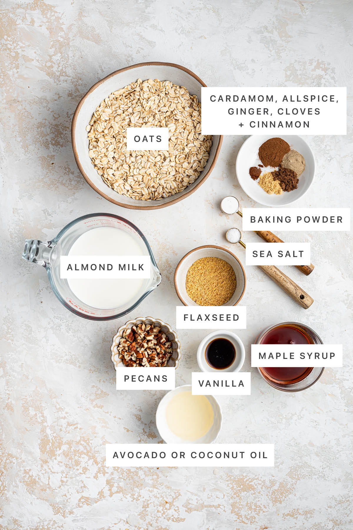 Ingredients measured out to make Chai Baked Oatmeal Cups: oats, cardamom, allspice, ginger, cloves, cinnamon, baking powder, sea salt, almond milk, flaxseed, pecans, vanilla, maple syrup and coconut/avocado oil.