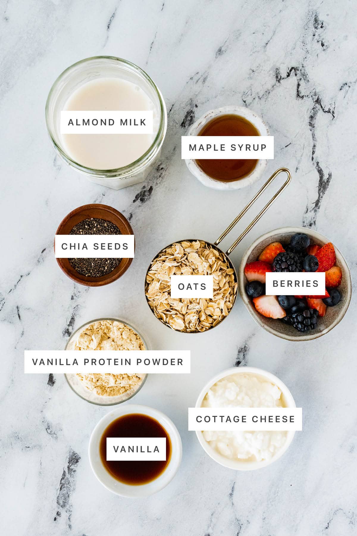 Ingredients measured out to make Cottage Cheese Overnight Oats: almond milk, maple syrup, chia seeds, oats, berries, vanilla protein powder, cottage cheese and vanilla.