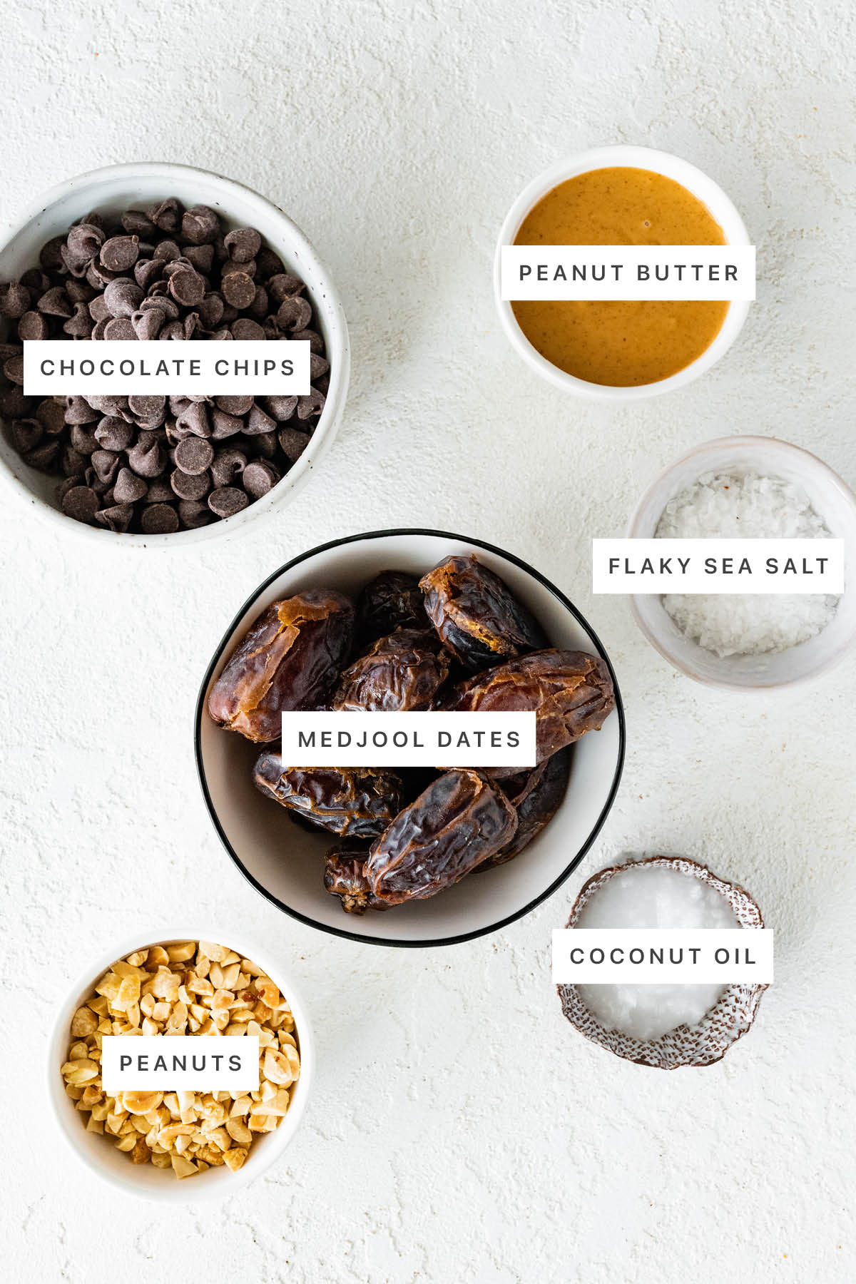 Ingredients measured out to make Date Bark: chocolate chips, peanut butter, flaky sea salt, medjool dates, peanuts and coconut oil.