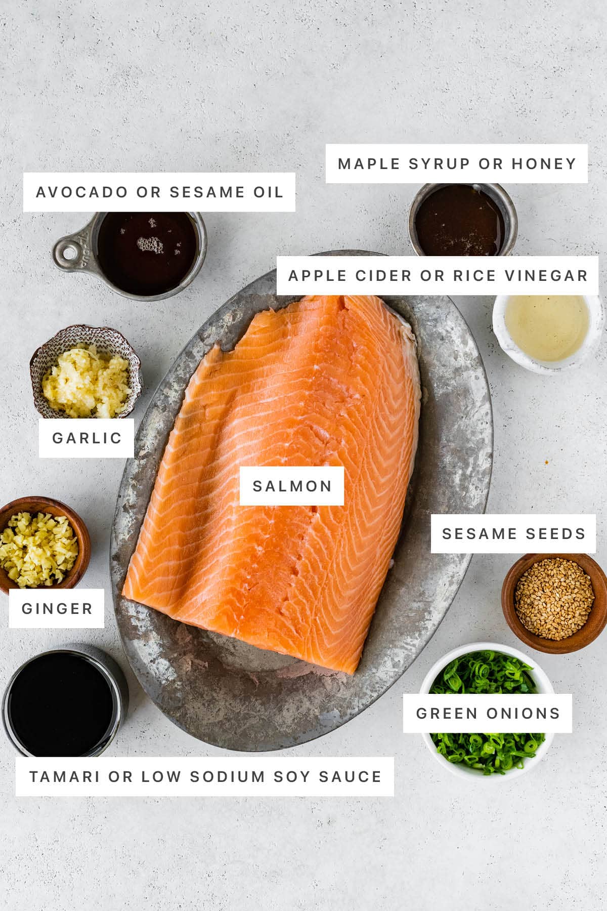 Ingredients measured out to make Air Fryer Salmon Bites: sesame oil, honey, rice vinegar, garlic, ginger, salmon, sesame seeds, tamari and green onions.