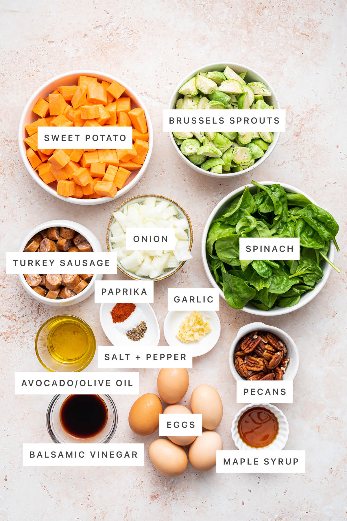 Ingredients measured out to make Sweet Potato Hash: sweet potato, brussels sprouts, onion, turkey sausage, spinach, paprika, garlic, salt, pepper, oil, balsamic vinegar, eggs, pecans and maple syrup.