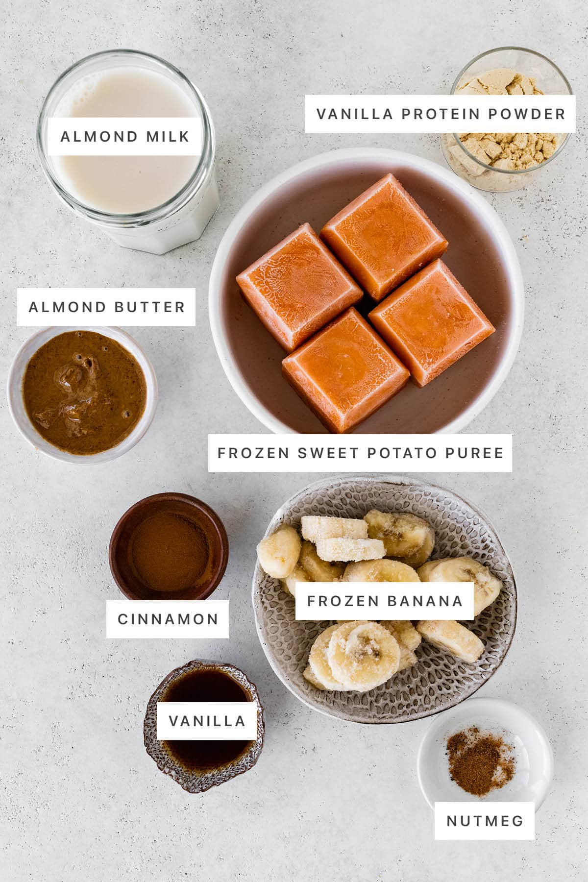 Ingredients measured out to make a Sweet Potato Smoothie: almond milk, vanilla protein powder, almond butter, frozen sweet potato puree, cinnamon, frozen banana, vanilla and nutmeg.