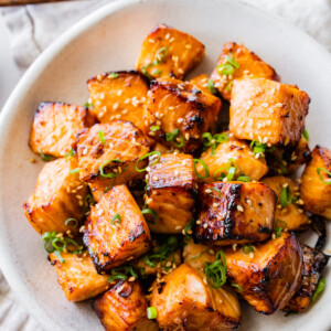 Air fryer salmon bites in a bowl garnished with sesame seeds and green onion.