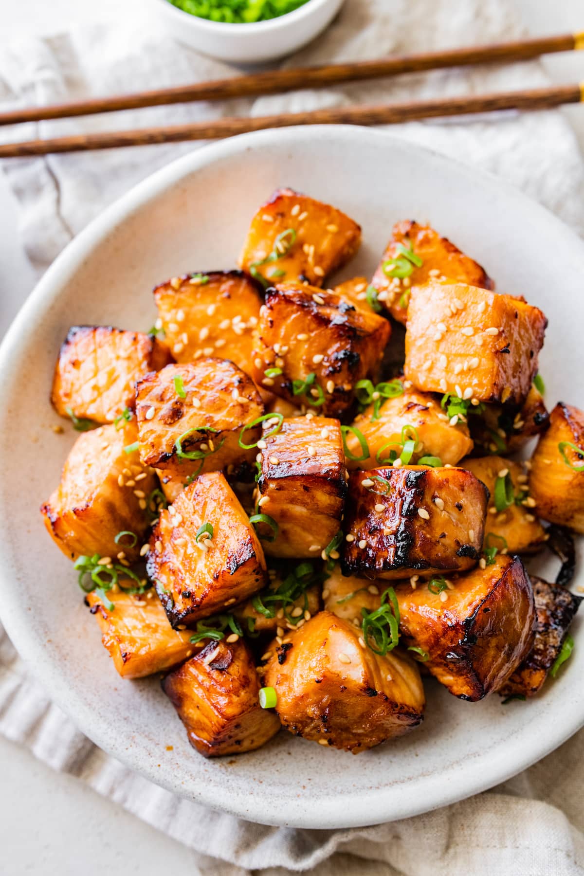 Air fryer salmon bites in a bowl garnished with sesame seeds and green onion.