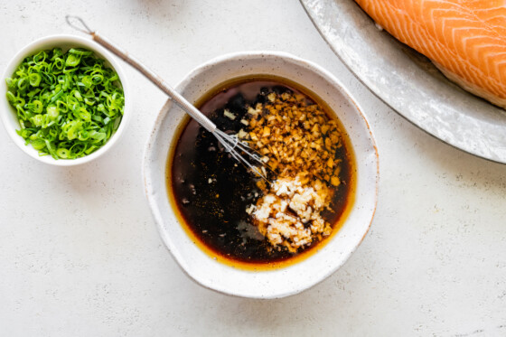 A small bowl with a metal whisk and oil, tamari, maple syrup, garlic, vinegar and ginger.