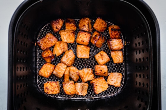 Salmon bites in an air fryer basket after being air fried.