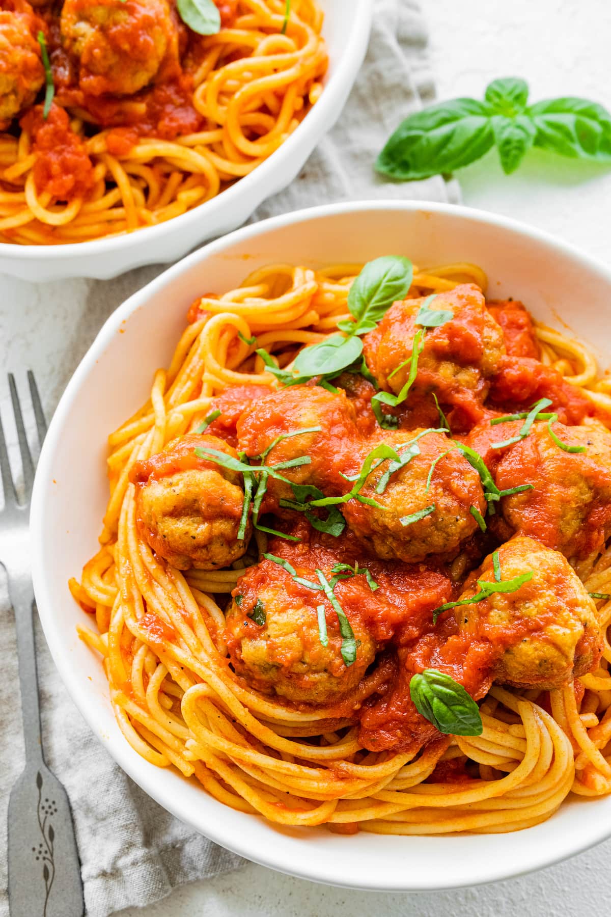 Baked turkey meatballs on spaghetti in a white bowl with marinara sauce.