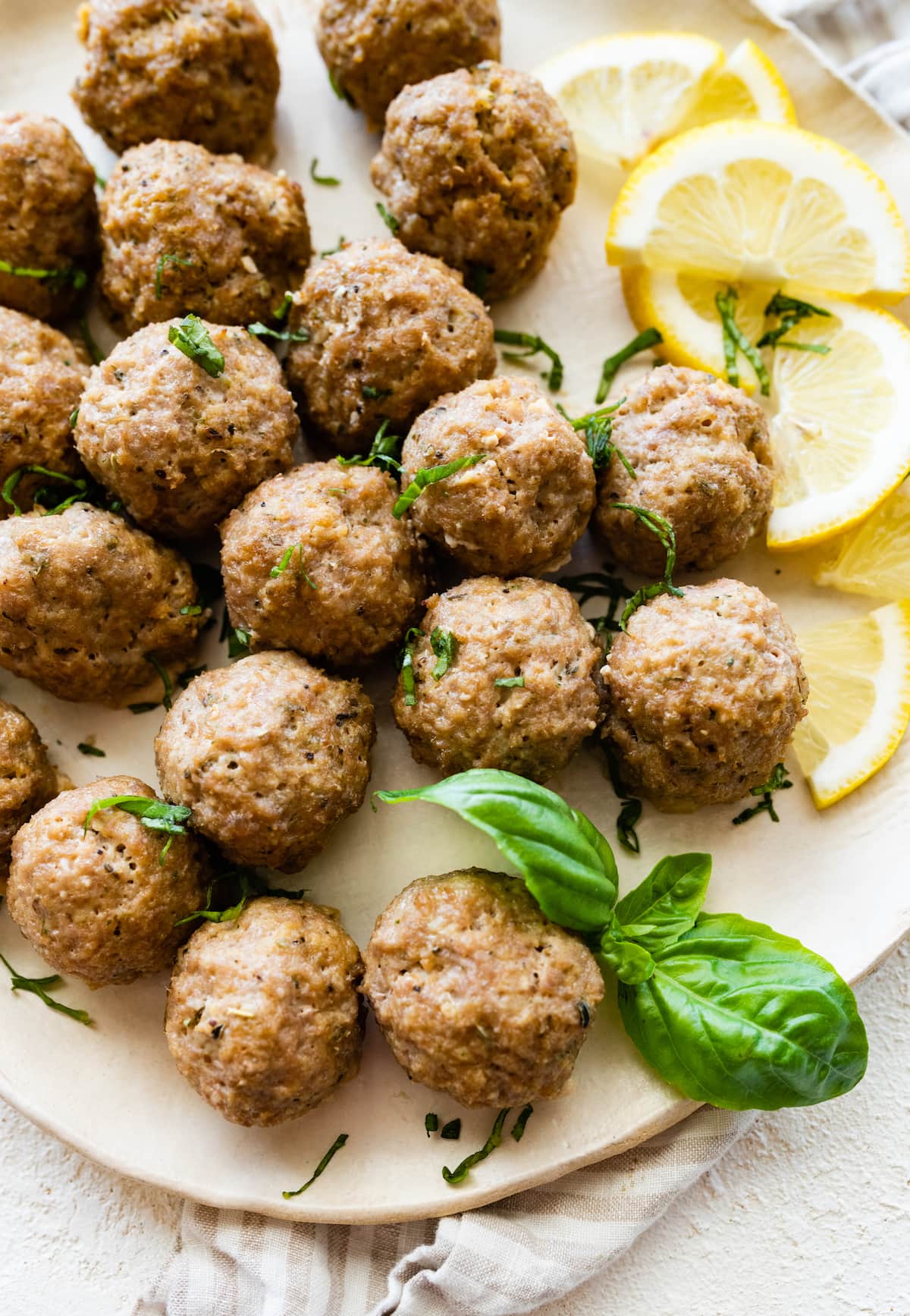 Baked turkey meatballs on a plate with fresh basil and lemon slices.