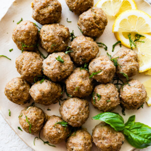 Baked turkey meatballs on a plate with fresh basil and lemon slices.