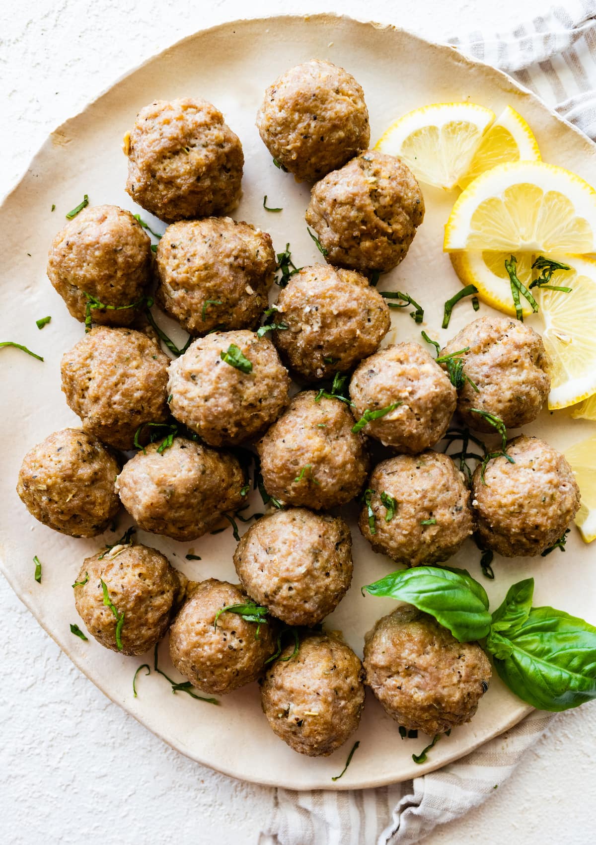 Baked turkey meatballs on a plate with fresh basil and lemon slices.