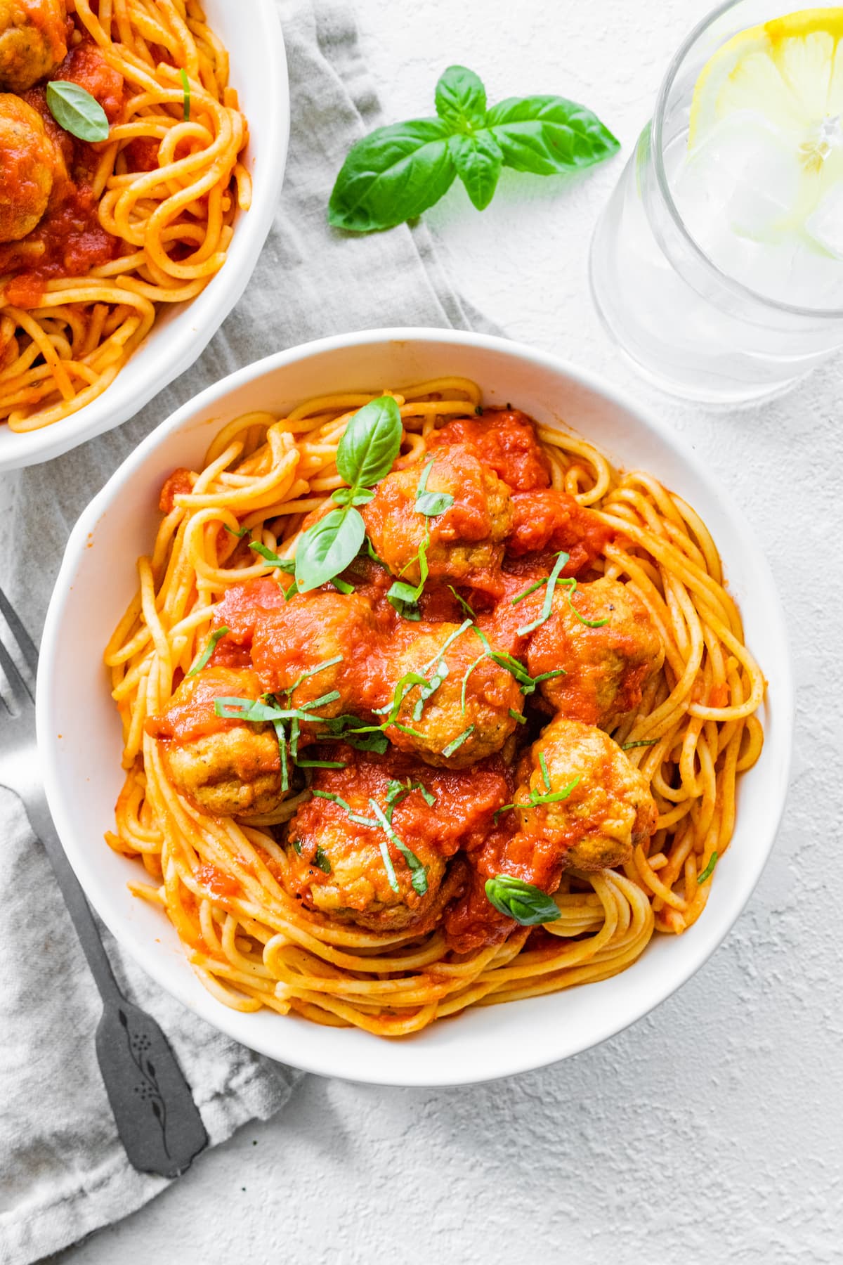 Baked turkey meatballs on spaghetti in a white bowl with marinara sauce.