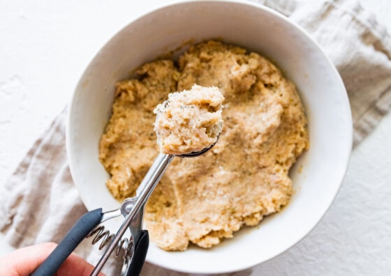 A cookie scoop with a portion of the baked turkey meatball mixture over a large white bowl.