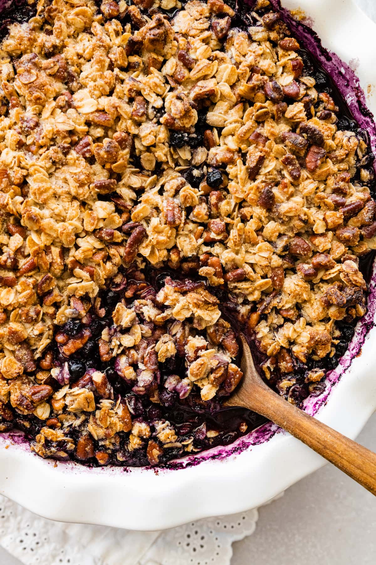 Blueberry crumble in a pie dish with a wooden spoon.