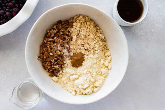 A large mixing bowl with flour, rolled oats, ground cinnamon, and pecans.