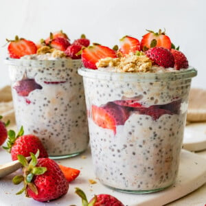 Two mason jars with strawberry cheesecake overnight oats topped with fresh strawberries.