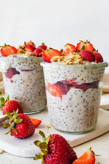 Two mason jars with strawberry cheesecake overnight oats topped with fresh strawberries.