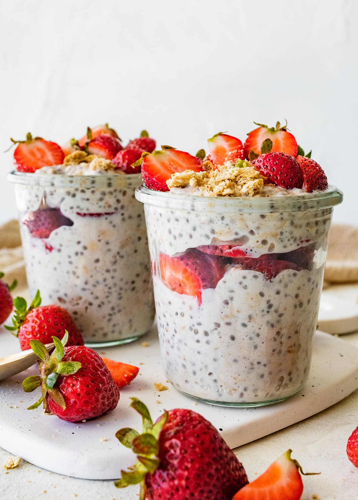 Two mason jars with strawberry cheesecake overnight oats topped with fresh strawberries.