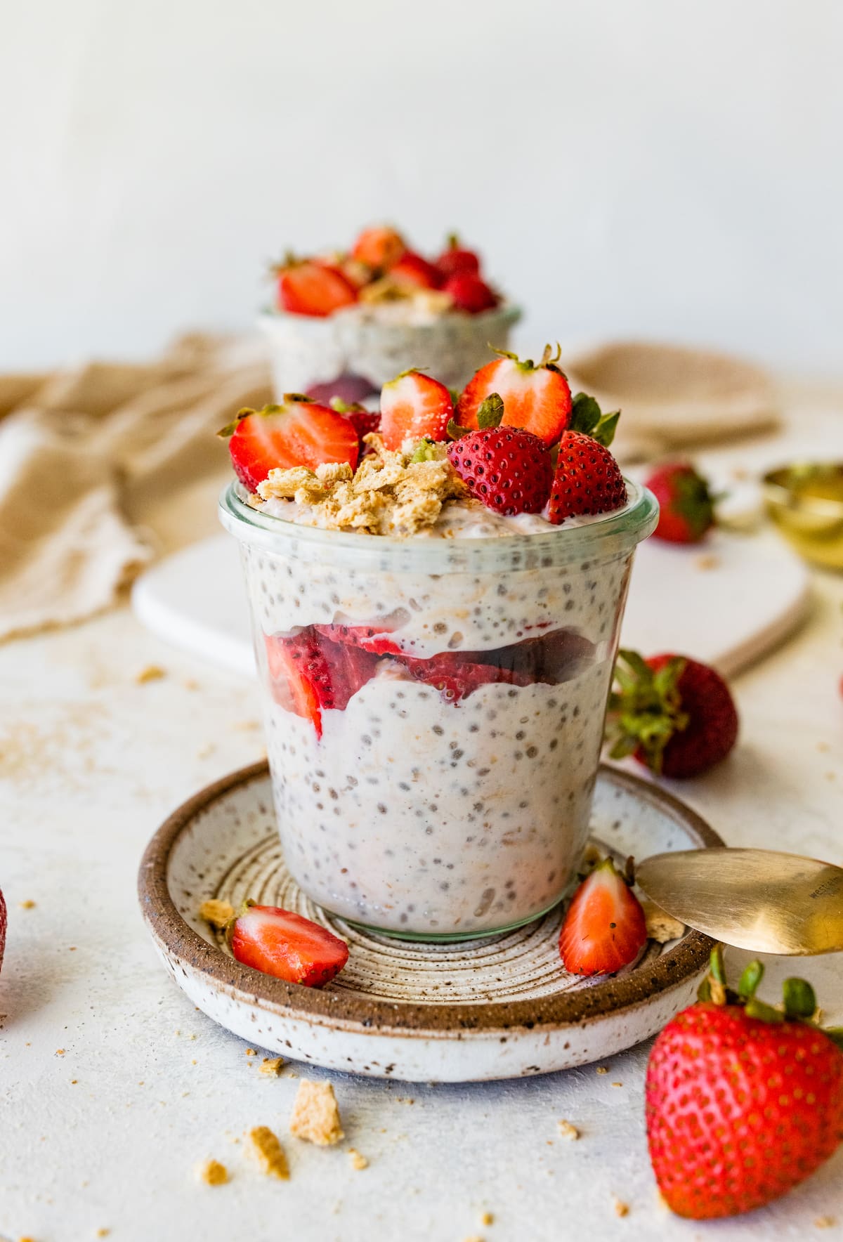 A mason jar on a small plate with strawberry cheesecake overnight oats and topped with fresh strawberries.