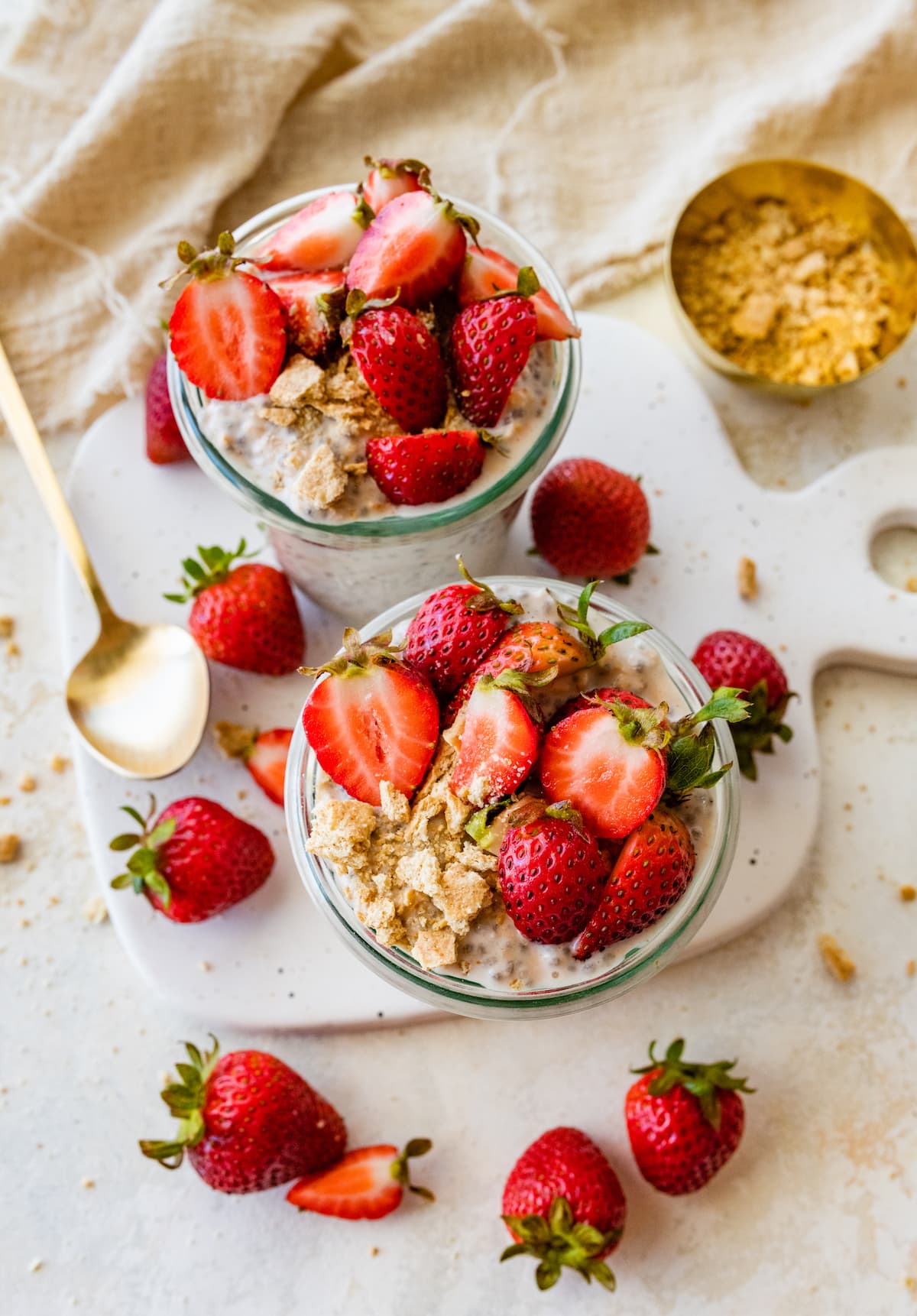 Two mason jars with strawberry cheesecake overnight oats topped with fresh strawberries.