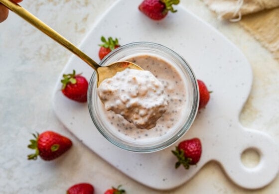 A spoonful of strawberry cheesecake overnight oats being held over a mason jar.