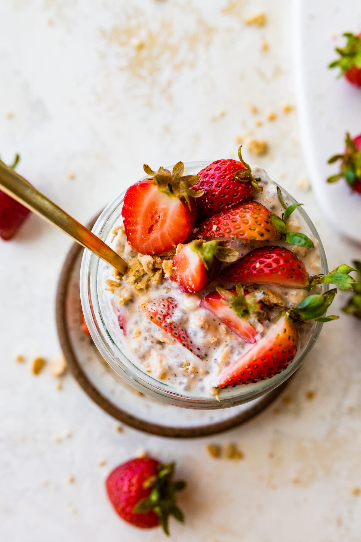 A mason jar with strawberry cheesecake overnight oats with a metal spoon and topped with fresh strawberries.