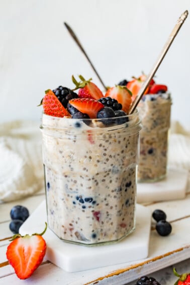 Two mason jars with cottage cheese overnight oats with metal spoons and topped with fresh berries.