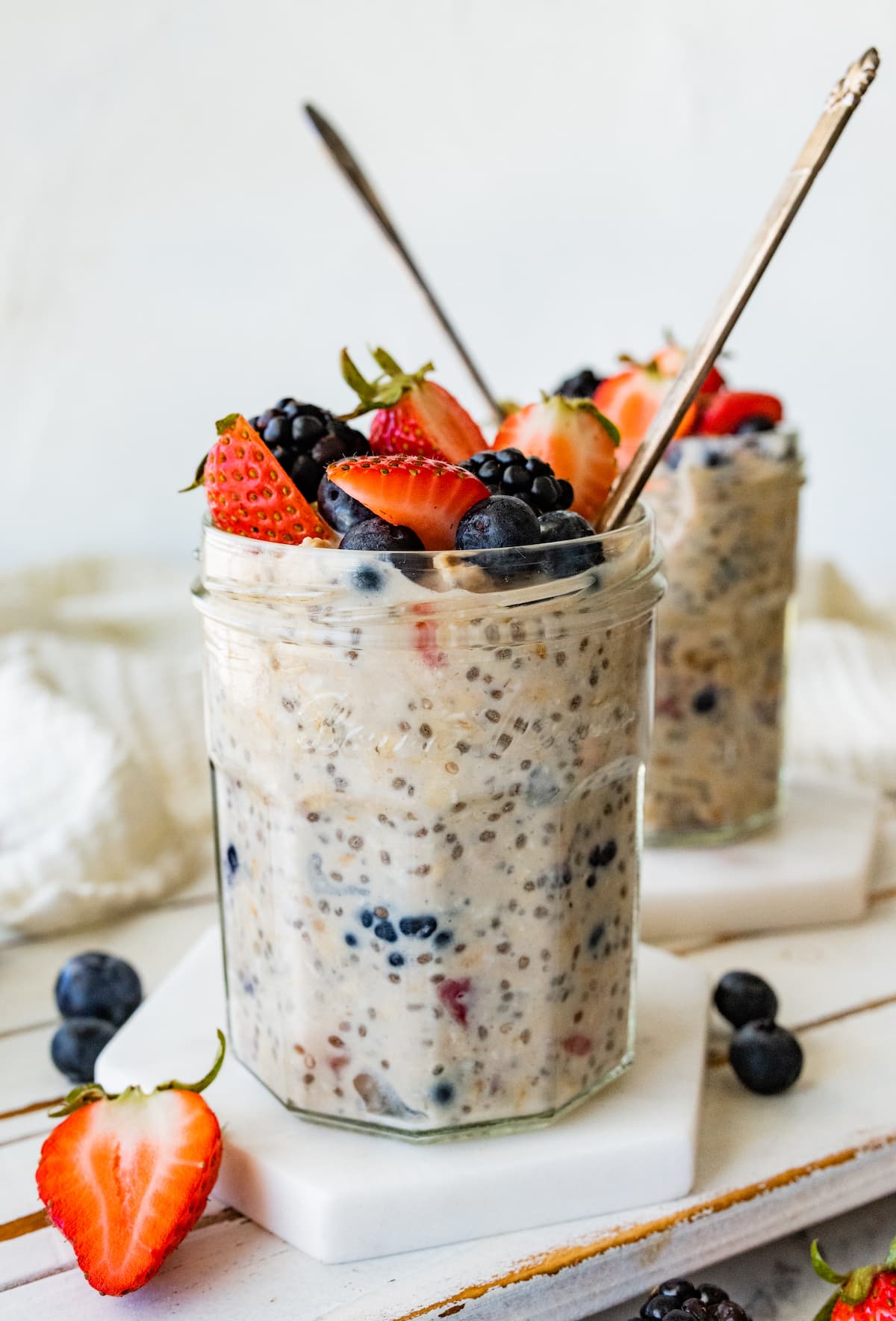 Two mason jars with cottage cheese overnight oats with metal spoons and topped with fresh berries.