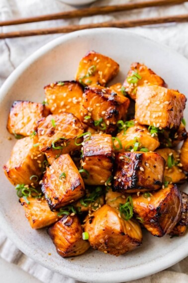 Air fryer salmon bites in a bowl garnished with sesame seeds and green onion.