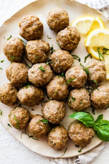 Baked turkey meatballs on a plate with fresh basil and lemon slices.