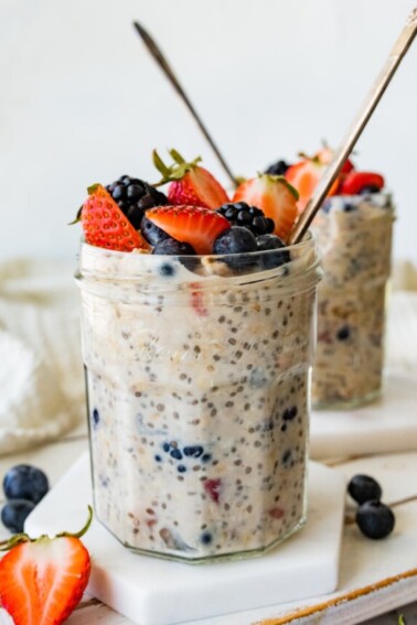 Two mason jars with cottage cheese overnight oats with metal spoons and topped with fresh berries.