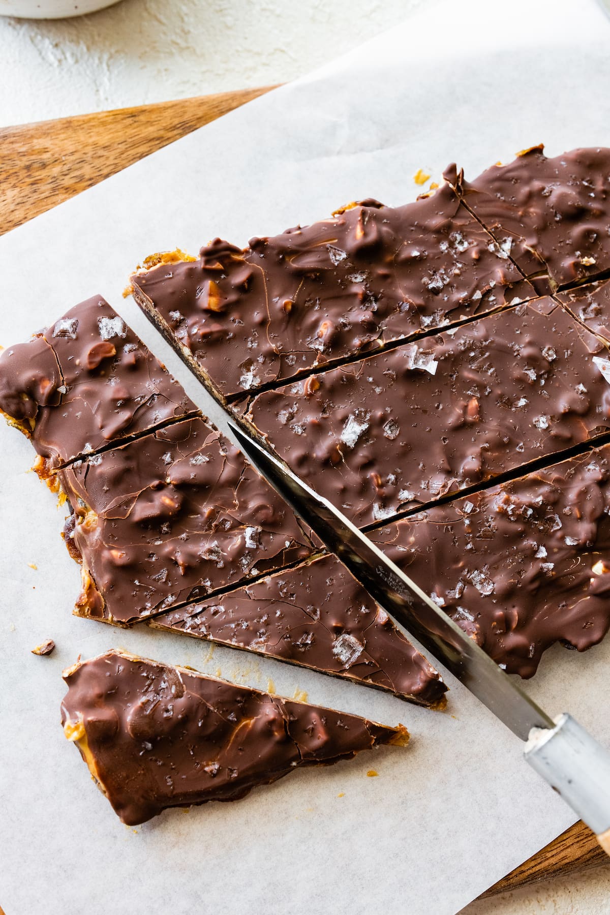 Date bark on parchment paper being cut into multiple pieces with a knife.