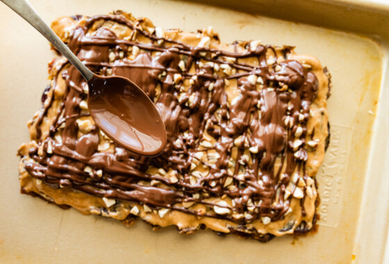 A metal spoon being used to drizzle chocolate on top of the peanut butter and dates.