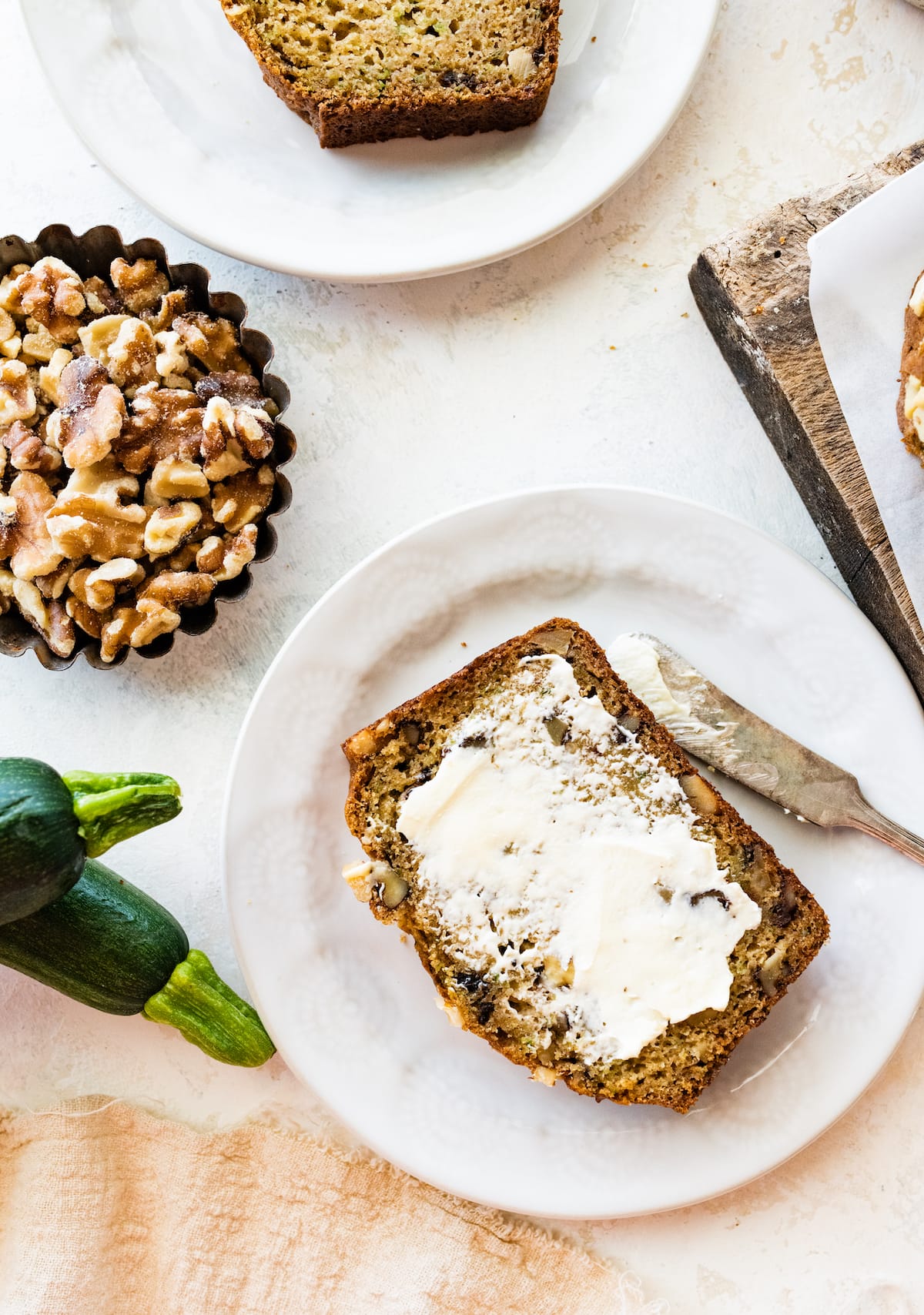 A slice of healthy zucchini bread on a white plate spread with butter.