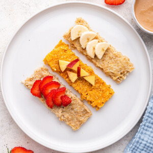 Three oatmeal fingers (banana, sweet potato and applesauce) on a white plate topped with fresh fruit.