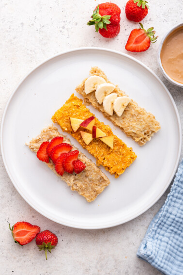 Three oatmeal fingers (banana, sweet potato and applesauce) on a white plate topped with fresh fruit.