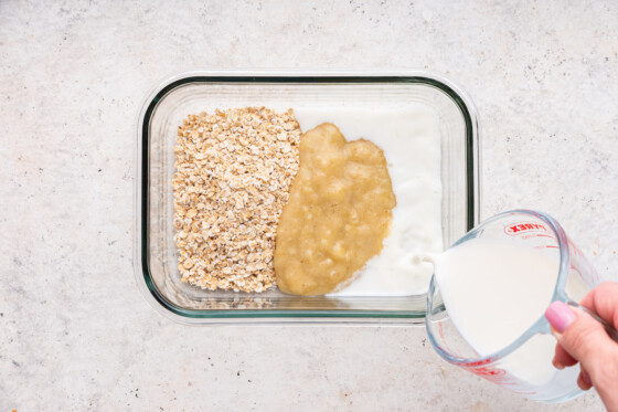 A woman's hand pouring milk into the oat and mashed banana mixture to make the oatmeal fingers.