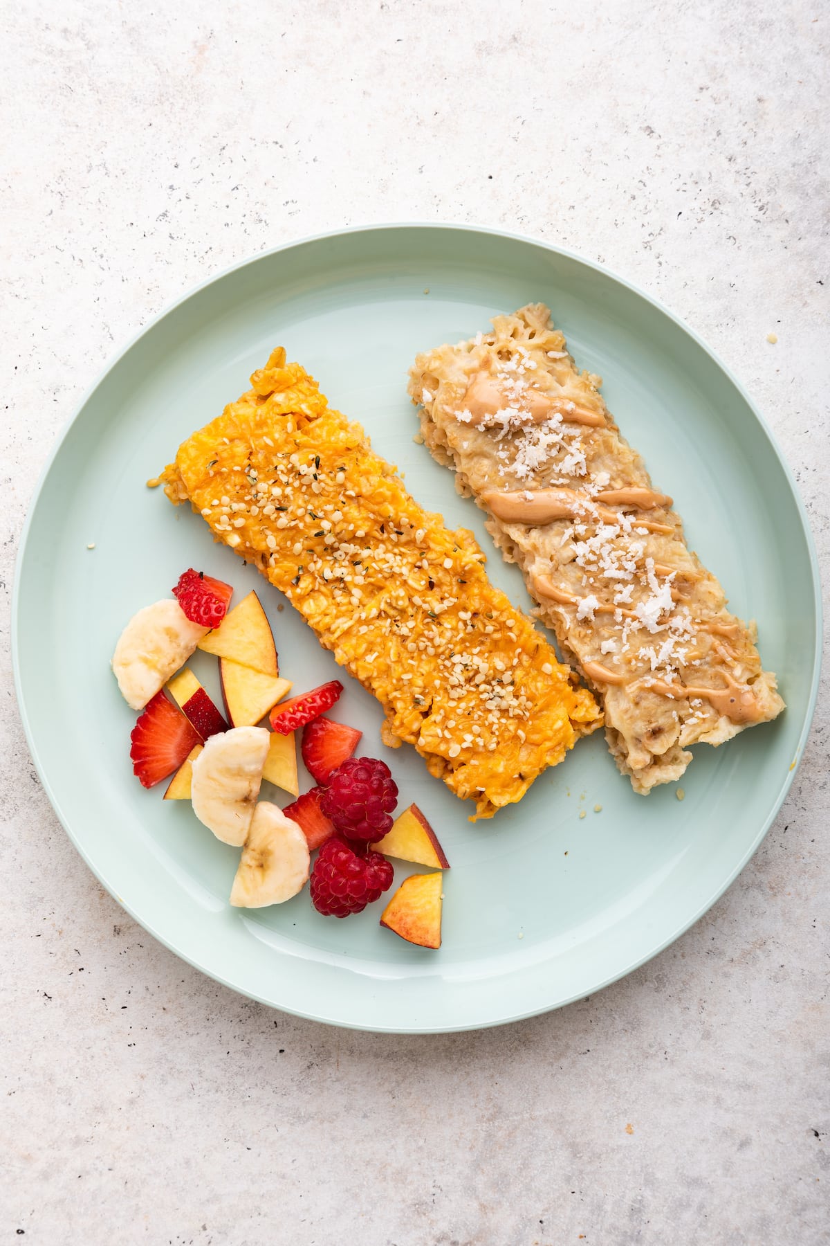 One sweet potato oatmeal finger and one applesauce oatmeal finger on a plate served alongside fresh fruit.