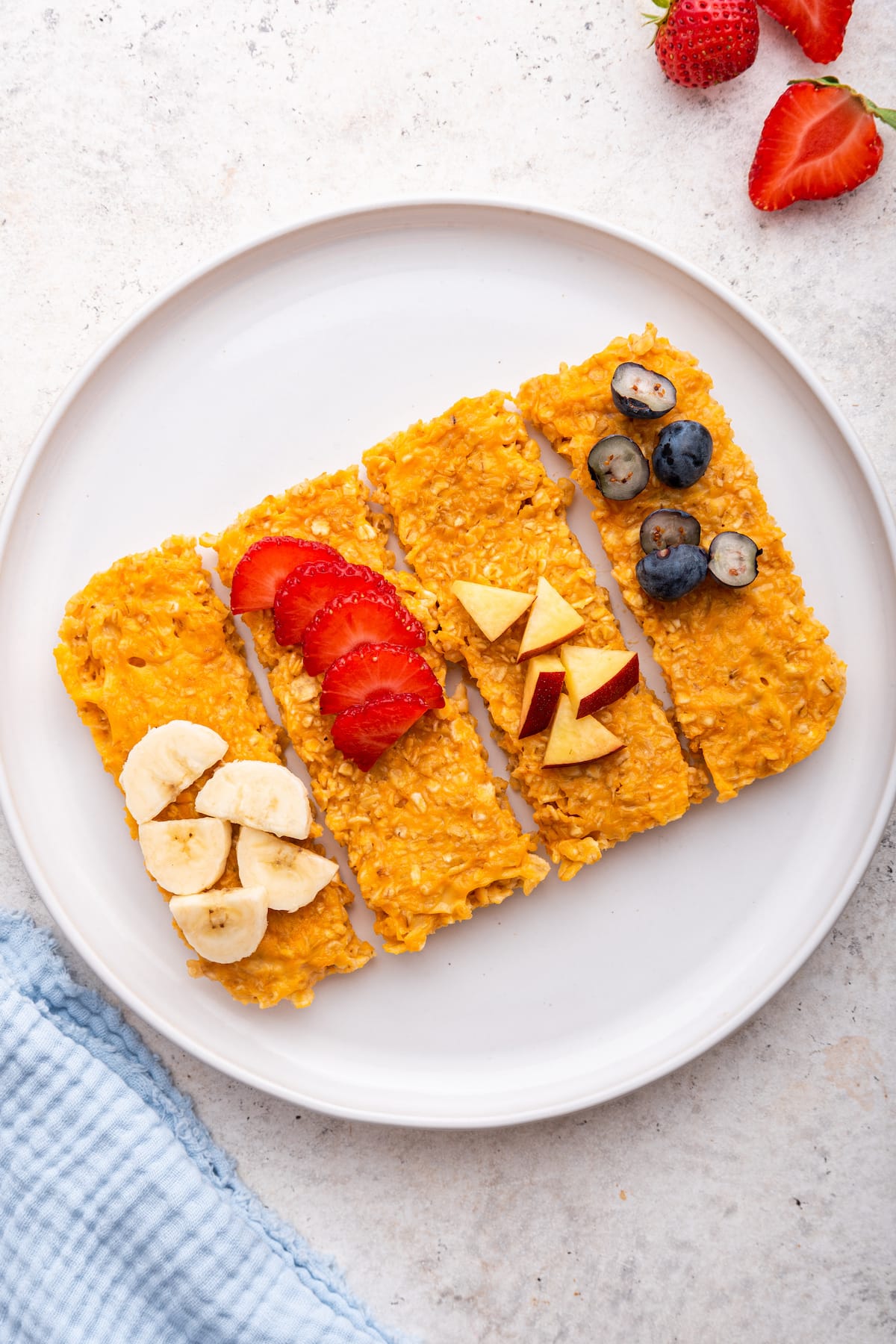 Four sweet potato oatmeal fingers on a plate topped with fresh fruit.