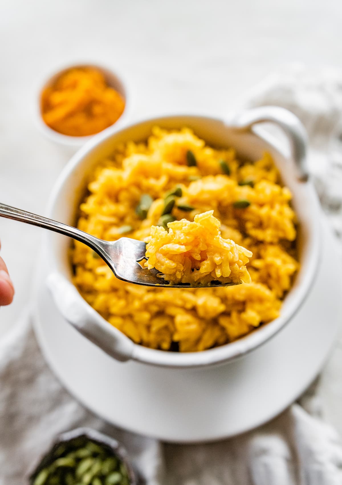 A fork holding a bite size portion of pumpkin rice over a small white bowl.