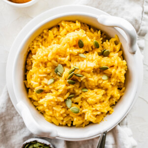 Pumpkin rice in a white bowl topped with pumpkin seeds.