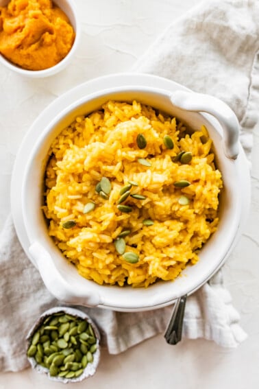 Pumpkin rice in a white bowl topped with pumpkin seeds.