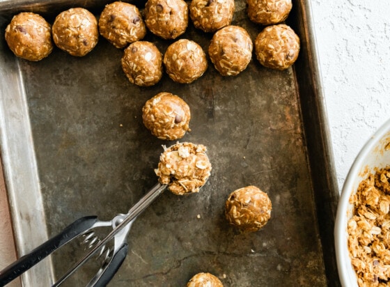 A cookie scoop forming the vegan protein balls on to a baking tray.